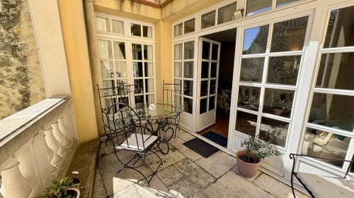 Terrasse ombragée à Entre vignes et dentelles avec mobilier en fer forgé, plantes en pots et portes-fenêtres à Courthézon