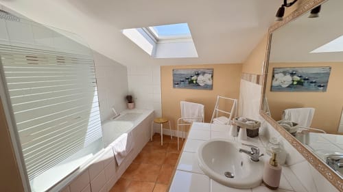 Salle de bains spacieuse de l'appartement Prince d'Orange à Entre vignes et dentelles, baignoire, lavabo, puits de lumière, tons pêche