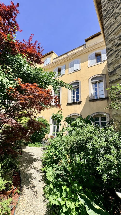 Charmante cour en pierre jaune à l'hôtel Entre vignes et dentelles à Courthézon, entourée de végétation luxuriante et de rouge