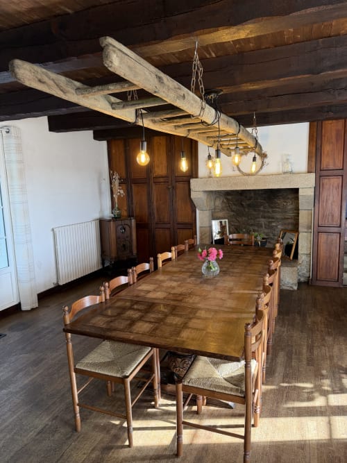 Salle à manger rustique du gîte Domaine de Lann Kerhuerh avec table en bois, chaises, plafond à poutres et luminaires vintage