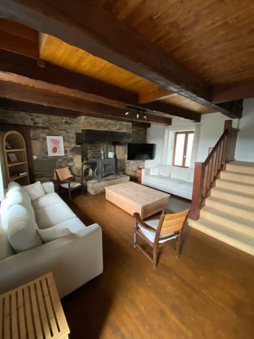 Grand salon avec poutres apparentes, cheminée en pierre, canapés blancs, table en bois et escalier au Domaine