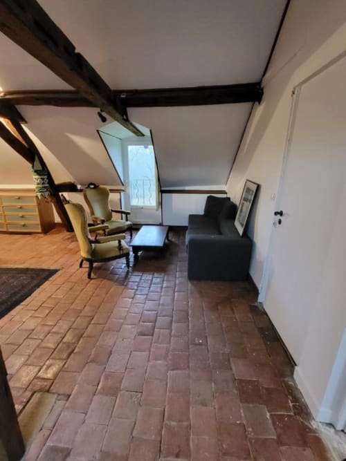 Salon mansardé dans la Chambre Quadruple d'Irancy au Domaine des Oiseaux de Passage, avec poutres apparentes, carrelage et tons crème