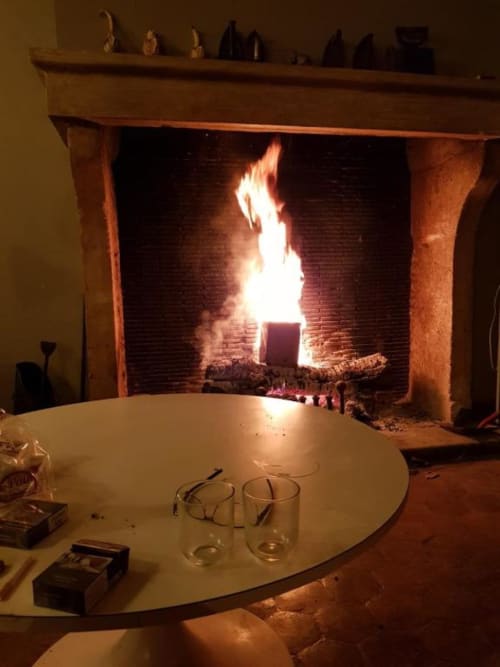 Foyer accueillant avec flammes actives au gîte DOMAINE DES OISEAUX DE PASSAGE, table ronde et verres au premier plan
