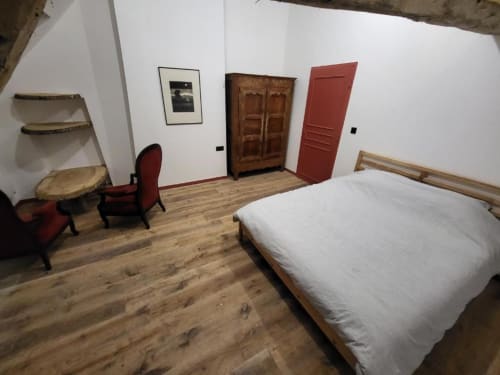 Chambre spacieuse du DOMAINE DES OISEAUX DE PASSAGE avec plancher en bois, literie blanche, fauteuil rouge et armoire en bois