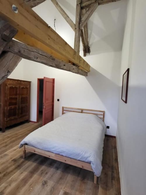 Chambre rustique du Domaine des Oiseaux avec poutres en bois, murs blancs, lit simple, porte rouge et mobilier en bois