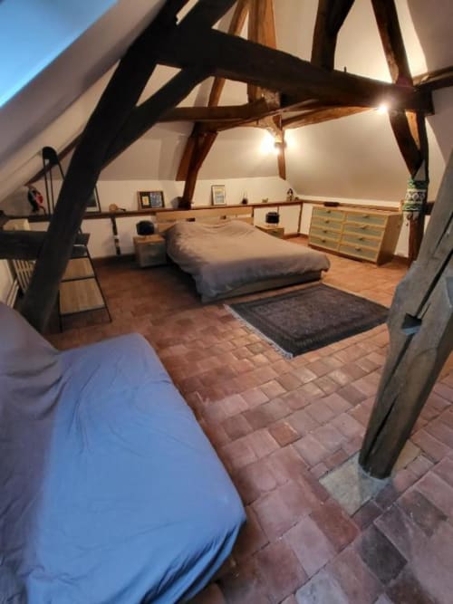Chambre spacieuse sous les combles avec poutres apparentes, deux lits, carrelage en terre cuite et vue sur le jardin