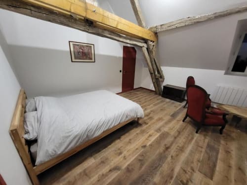 Chambre spacieuse sous les combles au DOMAINE DES OISEAUX DE PASSAGE avec poutres apparentes, lit queen-size, fauteuil rouge et parquet