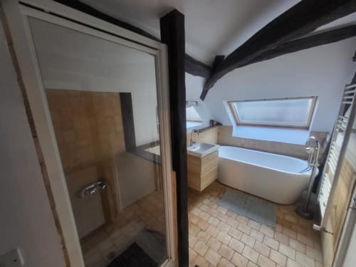 Salle de bains moderne avec baignoire îlot, douche, puits de lumière, poutres apparentes et vue sur jardin à Domaine des Oiseaux de Passage
