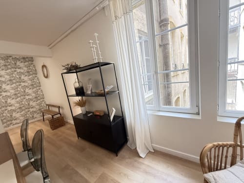 Appartement moderne à Metz avec étagères noires, mobilier en bois et vue sur la ville par grandes fenêtres