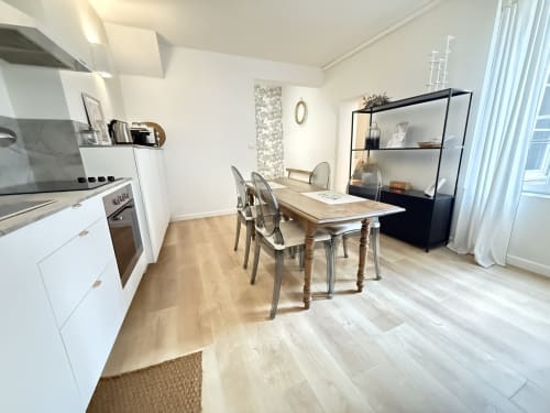 Cuisine-salle à manger moderne dans un appartement de Metz avec table en bois, chaises transparentes, mobilier blanc et étagère noire