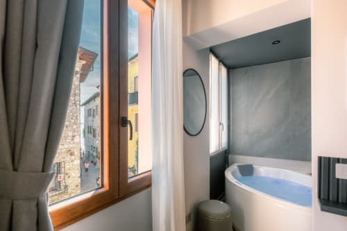 Bagno moderno a Casa Giulietta a Como con vasca azzurra, specchio rotondo e finestra che affaccia sulla strada