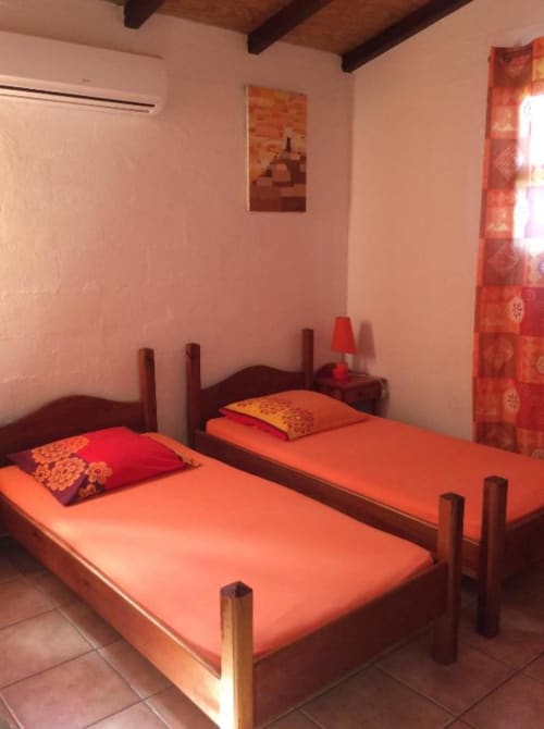 Deux lits jumeaux avec literie orange dans une chambre rose vif à l'Art Lodge Kafé, Bouillante Guadeloupe