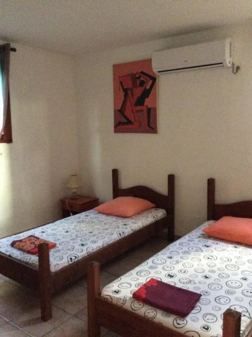 Chambre twin avec lits en bois, matelas à motifs souriants, oreillers corail et œuvres rouges à l'Art Lodge Kafé de Bouillante