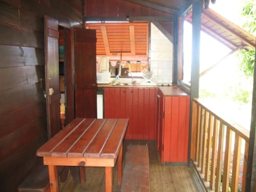 Terrasse du bungalow Mango avec table en bois, cuisine rouge et vue sur l'océan à Art Lodge Kafé, Bouillante