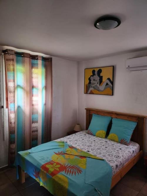 Chambre colorée dans un appartement guadeloupéen avec lit en bois, literie turquoise, rideaux à motifs et art mural abstrait
