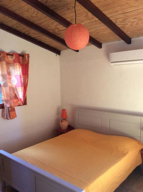 Chambre confortable à l'Art Lodge Kafé en Guadeloupe avec poutres apparentes, suspension rouge et literie orange