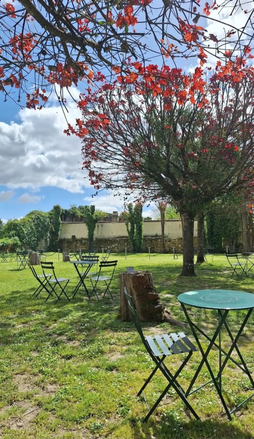 Outdoor garden seating at La Maison du Clocher in Saint-Emilion with red flowering tree and bistro tables
