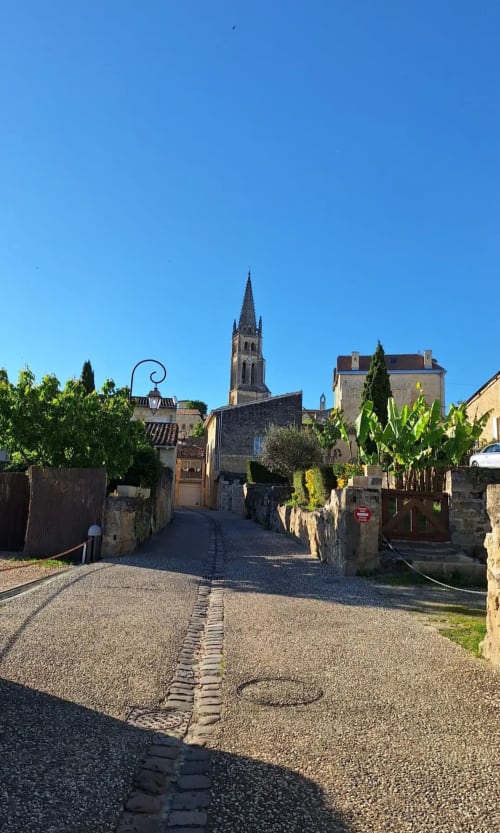 Charming street view in Saint-Emilion leading to church tower, featuring stone walls and green shutters at La Maison du