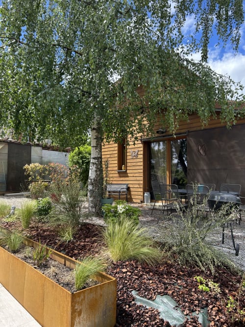 Patio rustique avec bouleau pleureur, salon de détente et jardinières aménagées à l'écolodge Les Papillons des Sucs