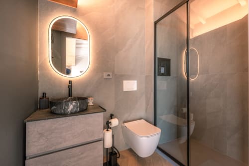 Bagno moderno alla Casa Giulietta a Como con specchio ovale illuminato, lavabo in marmo, wc bianco e doccia in vetro