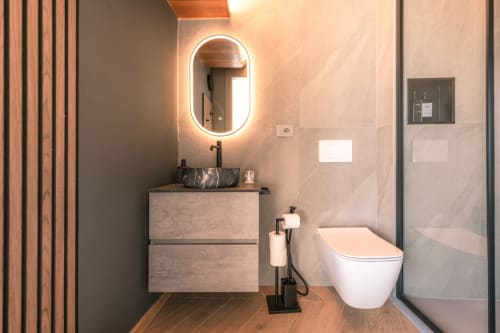 Bagno moderno a Casa Giulietta Como con specchio LED ovale, lavabo in marmo, WC bianco, dettagli in legno e vetro