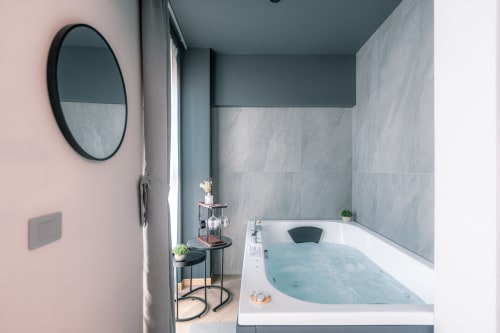 Bagno moderno presso Casa Giulietta Sirmione con vasca idromassaggio, piastrelle grigie, specchio circolare e parete accent rosa