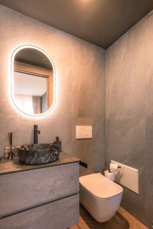 Bagno moderno a Casa Giulietta Sirmione con specchio ovale illuminato, lavabo in marmo nero, wc bianco e legno caldo