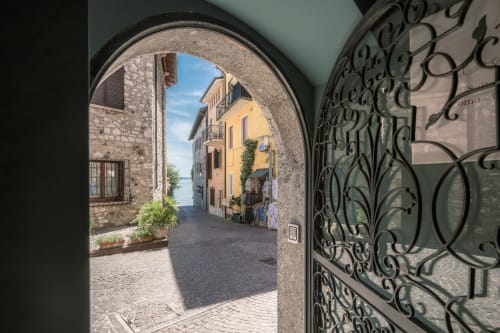 Cancello in ferro battuto che si apre su un affascinante vicolo italiano a Sirmione, Como, con edifici storici in pietra e vista sul lago