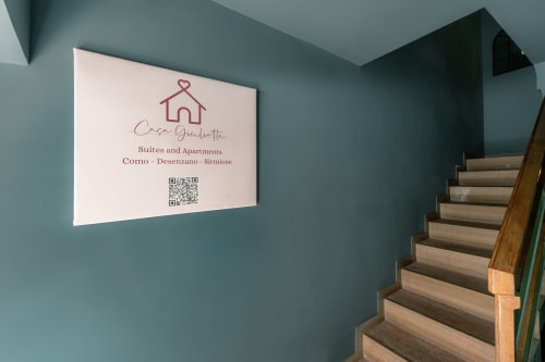Insegna Casa Giulietta nella scala color azzurro-verde con gradini in legno che conducono alle suite a Como, Sirmione