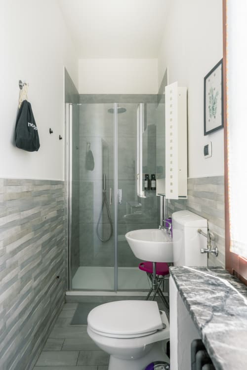 Bagno moderno nella camera Lilly di Casa Giulietta a Como, con doccia in vetro, lavabo bianco e finiture piastrellate neutre