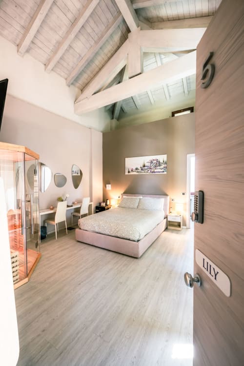 Camera Lilly a Casa Giulietta Como: camera da letto moderna con letto rosa, pavimenti in legno, specchi e soffitto con travi a vista