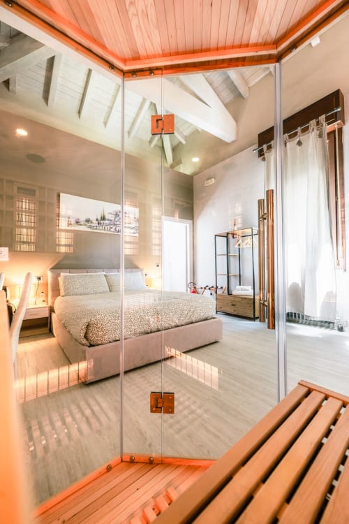 Camera Lilly di Casa Giulietta a Como con doccia moderna in vetro, travi arancioni al soffitto e vista sul letto