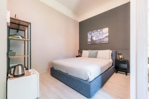 Camera da letto moderna a Casa Giulietta Como con letto blu, parete accent grigia, TV a schermo piatto e pavimento in legno