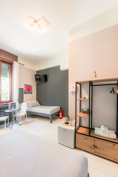 Camera moderna presso Casa Giulietta Como con letto singolo, parete accent verde, TV, minibar, scaffali in legno e vista sulla città