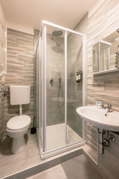Bagno moderno di Casa Giulietta Como con doccia aperta, lavabo bianco e pareti con piastrelle effetto legno orizzontale