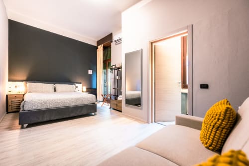 Camera da letto moderna a Casa Giulietta, Como con parete d'accento scura, letto queen, pavimenti in legno e cuscino decorativo giallo