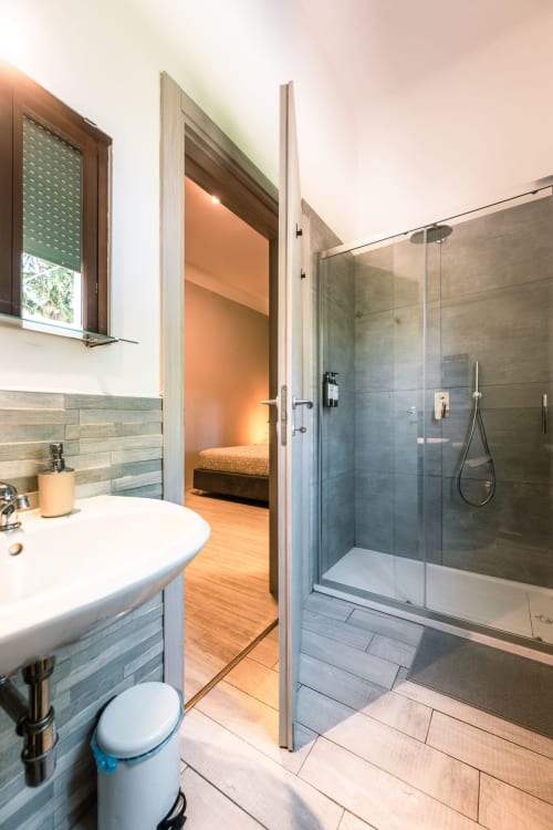 Bagno moderno a Casa Giulietta Como con doccia aperta, lavabo, wc e pavimentazione in legno