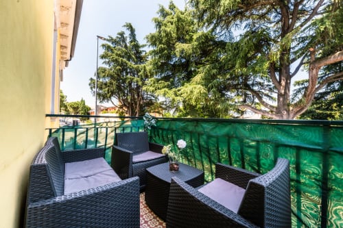Balcone di Casa Giulietta Como con sedute in vimini, schermo verde per la privacy e alberi alti che si affacciano sulla città