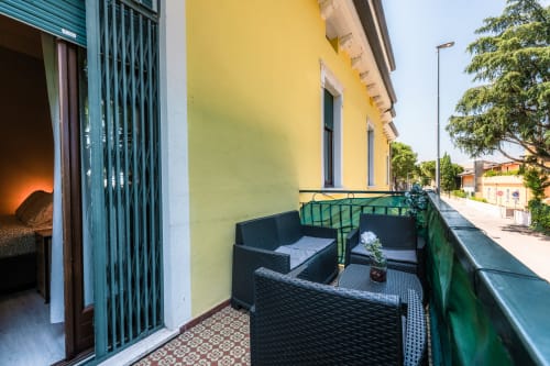 Balcone della camera Girasole a Casa Giulietta Como con sedute in rattan nero, parete gialla e vista sulla strada