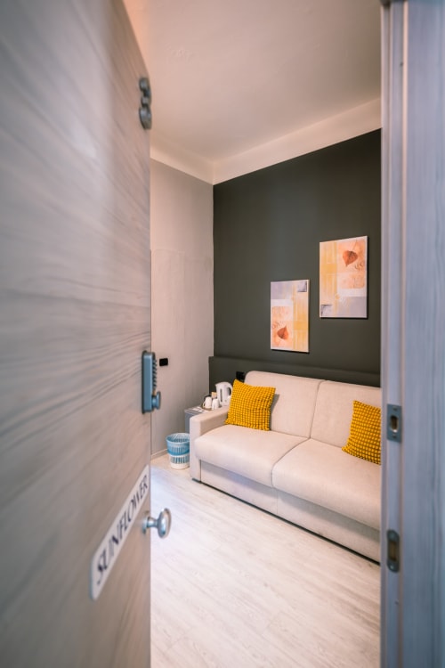 Camera da letto moderna a Casa Giulietta Como con divano crema, parete accent scura, cuscini gialli e opere d'arte contemporanea