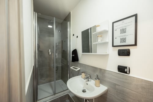 Bagno moderno della camera Ginger a Casa Giulietta, Como, con doccia a fondo aperto, lavabo bianco e dettagli in legno