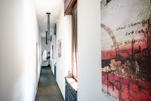 Stretto corridoio nella camera Ginger di Casa Giulietta a Como, con muri bianchi, opere d'arte e panca finestra