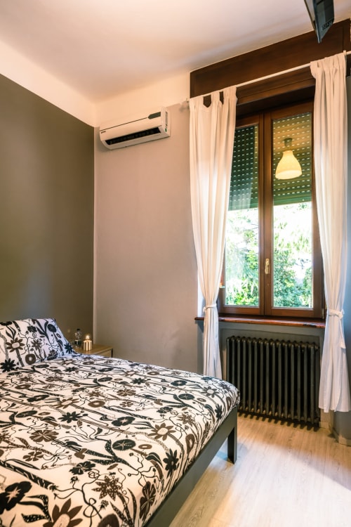 Camera viola a Casa Giulietta Como: letto con biancheria floreale, condizionatore, porte-finestre con vista sul lago, pavimento in legno