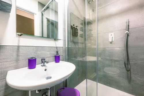 Bagno moderno dell'hotel Casa Giulietta Como con lavabo bianco, accessori viola, cabina doccia in vetro e specchio