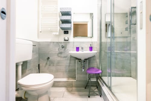 Bagno moderno in Casa Giulietta Como con lavabo bianco, WC, doccia walk-in, accenti viola e mobile vanity con specchio