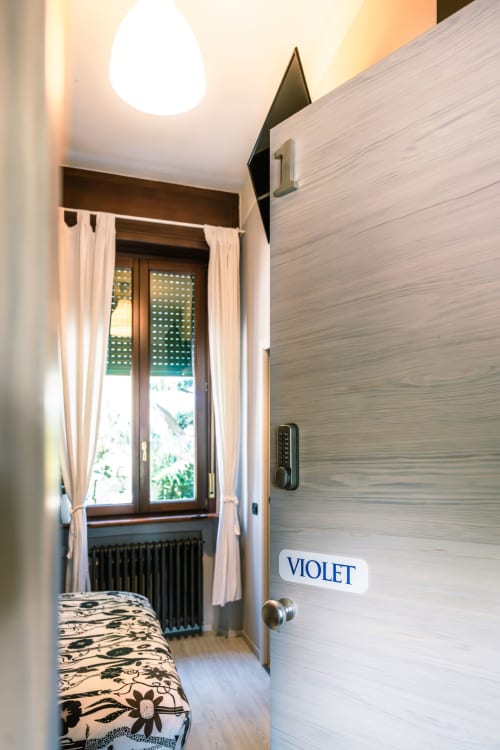 Corridoio d'ingresso della camera Violet a Casa Giulietta Como, con finestra, tende e serratura digitale sulla porta