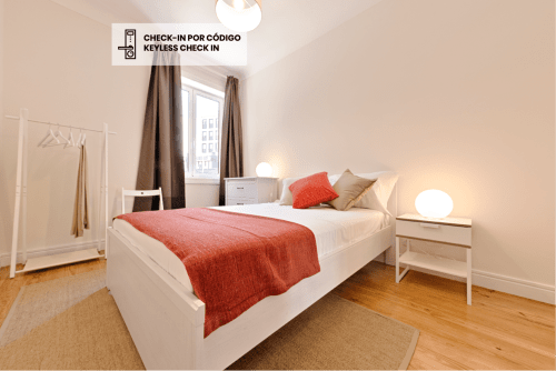 Modern bedroom in downtown Porto apartment with white bed, red accent blanket, wooden floors, and city view from window