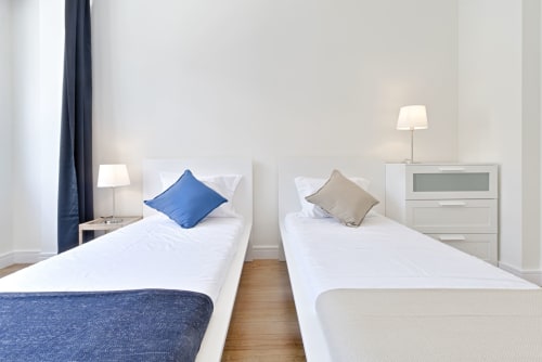 Twin bedroom in Porto city center apartment with white beds, blue and taupe pillows, wooden flooring, and modern furnishings