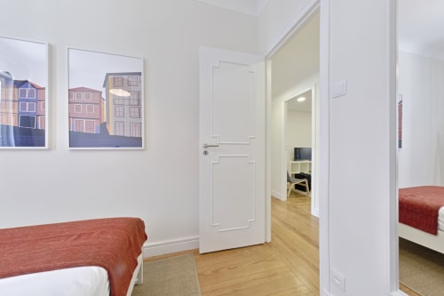 Modern apartment hallway in downtown Porto with wooden floors, white doors, and city view artwork on walls
