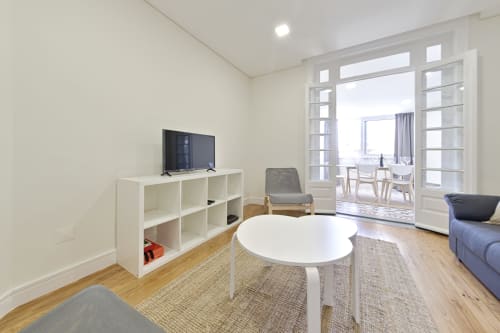 Sala de estar moderna em apartamento no centro do Porto com prateleiras brancas, mesa redonda, TV e vista da cidade através de portas de vidro